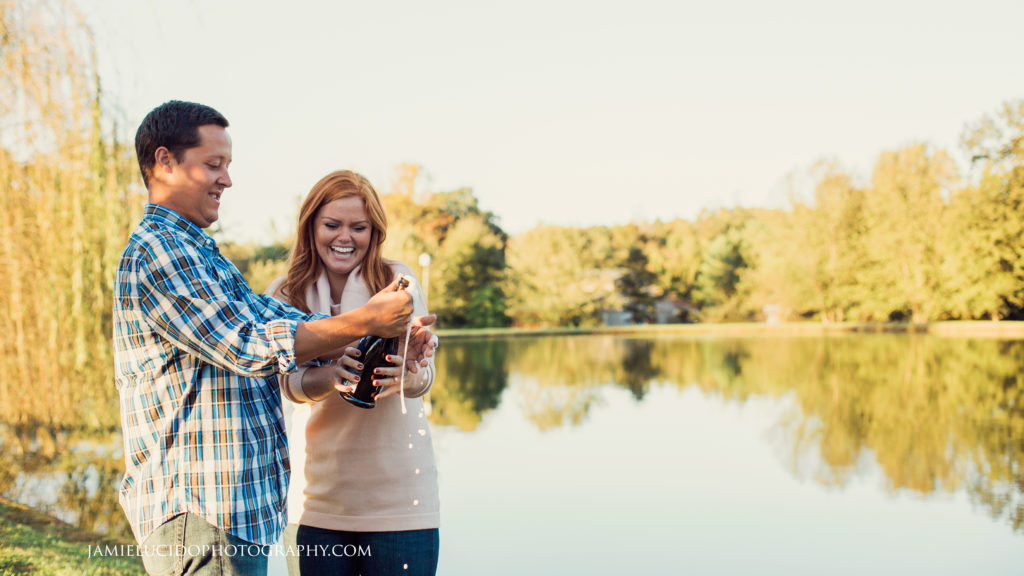 engaged couple pops champagne by lake at morning glory farm